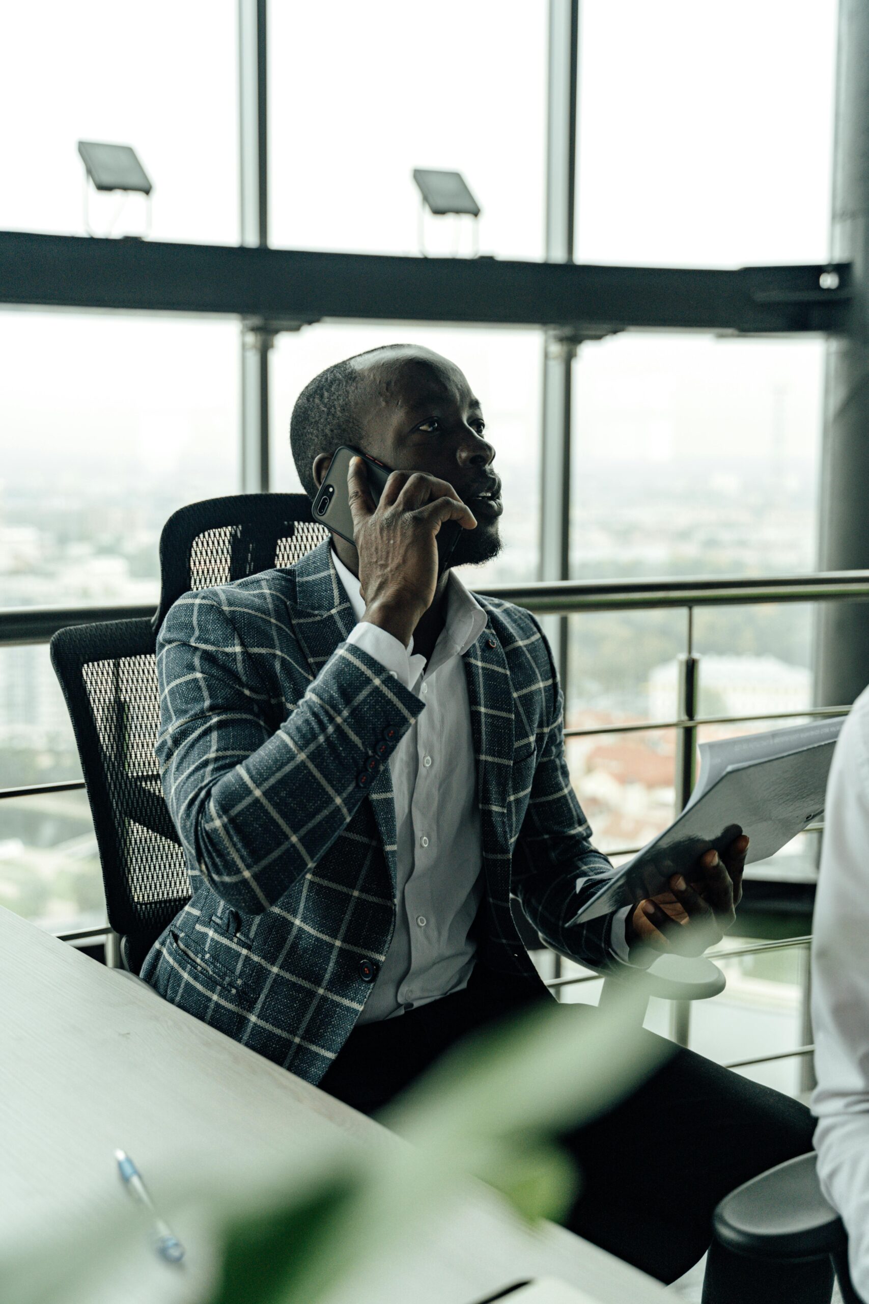 Focused businessman talking on smartphone while holding a document in a modern office setting.